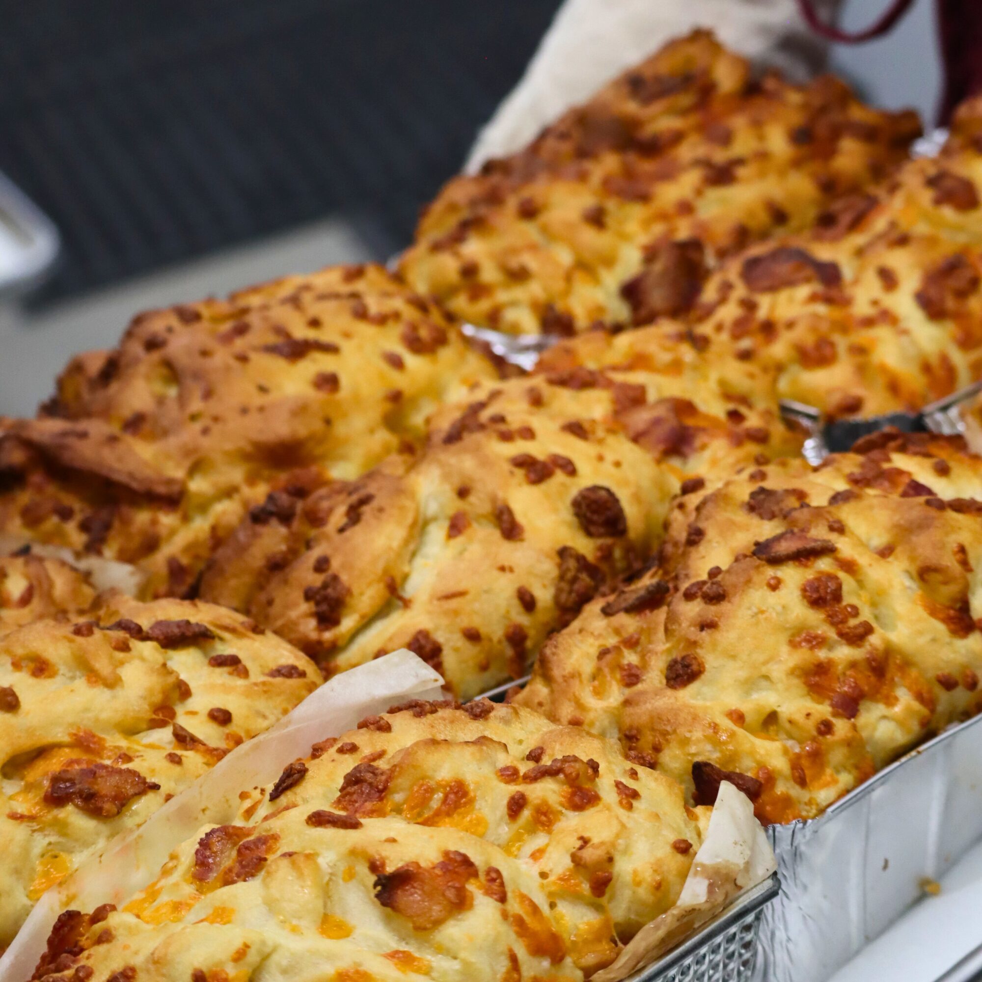 Freshly baked loaves of cheese bread with golden, crispy tops sit in metal trays, arranged closely together, showcasing their textured, cheesy crusts.